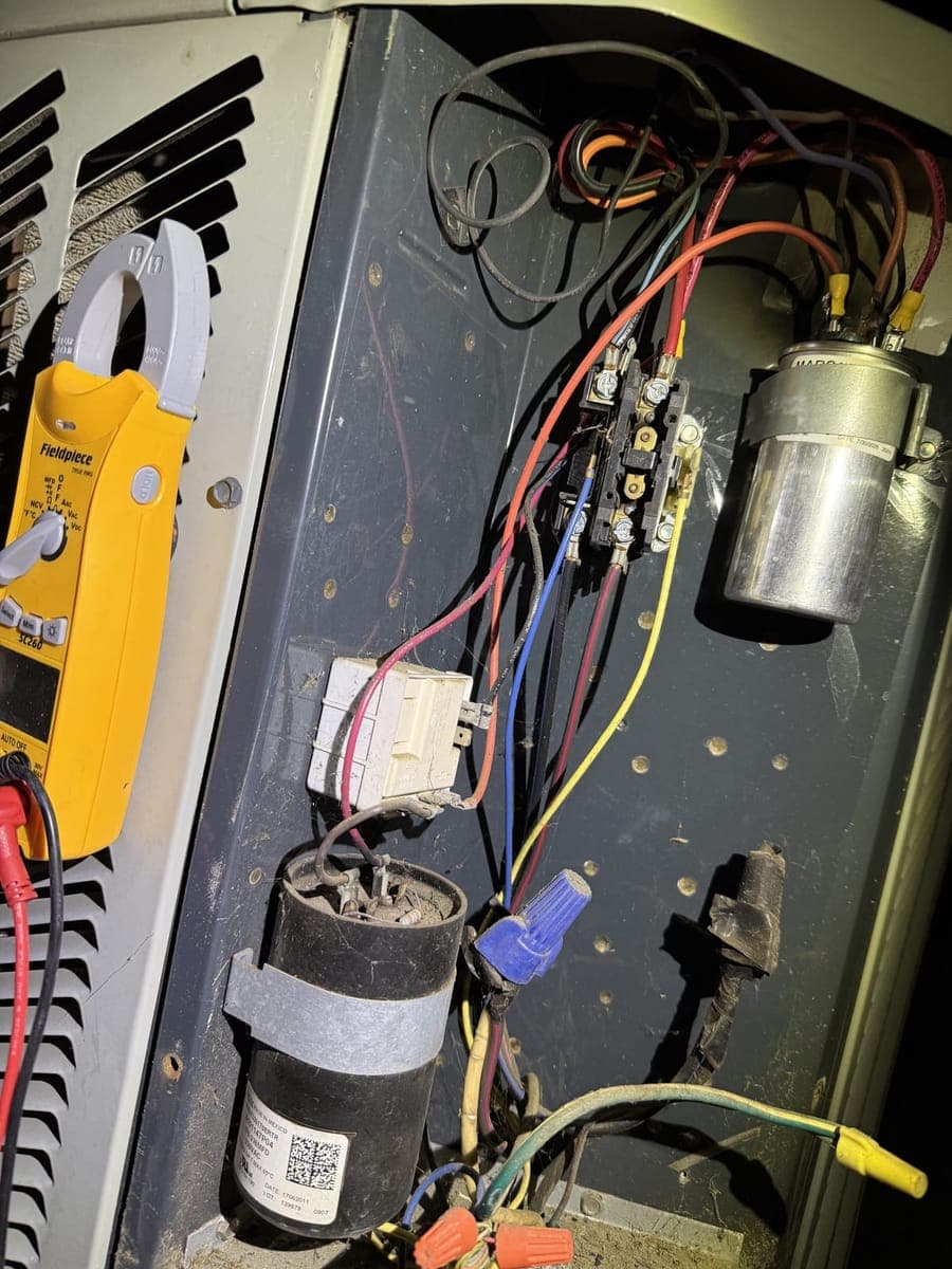 Open outdoor unit electrical panel with a capacitor, contactor, and a clamp meter connected