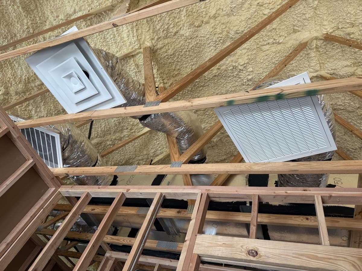 Square ceiling diffusers and a return grille set into ceiling framing, with flex duct above