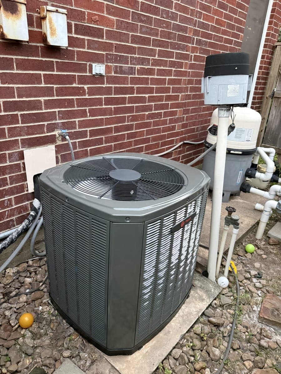 New Trane outdoor condenser on a pad against a brick wall