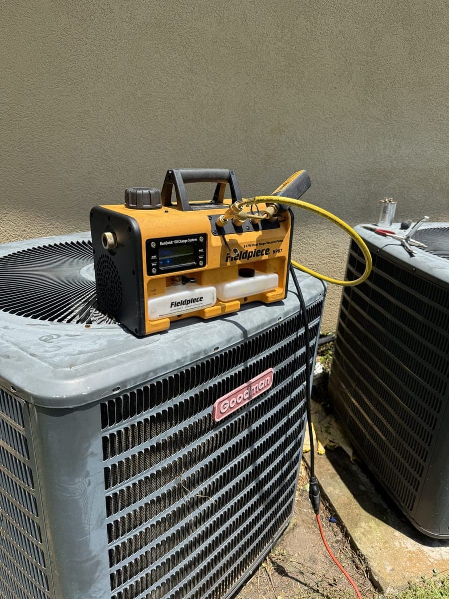 Yellow vacuum pump sitting on top of an outdoor AC unit with hoses connected
